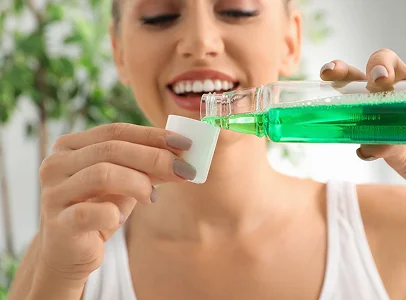 Femme souriante versant du bain de bouche vert dans un gobelet doseur à Montgiscard en Haute-Garonne 31