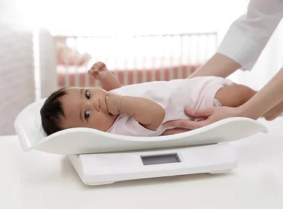 Bébé sur une balance, regardant l'appareil photo, mains d'adulte le soutenant à Montgiscard en Haute-Garonne 31