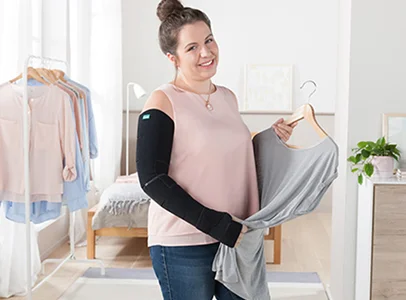 Femme souriante avec un manchon de bras noir tenant un cintre avec un t-shirt gris à Montgiscard en Haute-Garonne 31