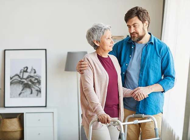 Un homme aide une femme âgée avec un déambulateur, souriant mutuellement à Montargis en Haute-Garonne 31