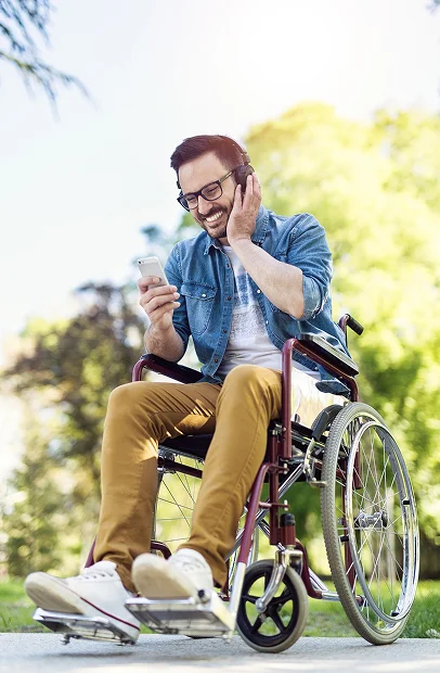 Homme souriant en fauteuil roulant, écoutant de la musique avec son téléphone en extérieur à Montgiscard en Haute-Garonne 31