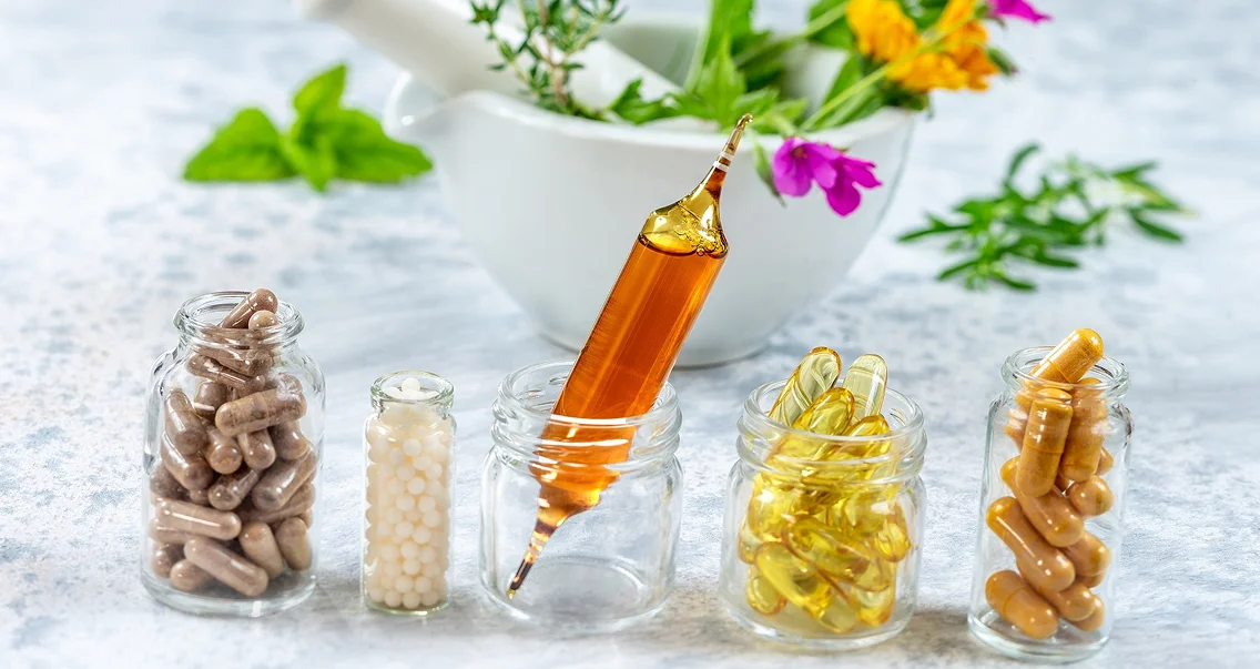 Cinq pots de compléments alimentaires, un mortier avec des herbes en arrière-plan.