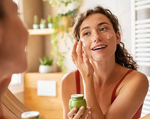 Femme souriante avec des taches de crème sur le visage, se regardant dans le miroir à Montgiscard en Haute-Garonne 31